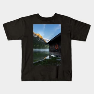 Boathouse with lifesaver Portrait. Amazing shot of a wooden house in the Ferchensee lake in Bavaria, Germany, in front of a mountain belonging to the Alps. Scenic foggy morning scenery at sunrise. Kids T-Shirt